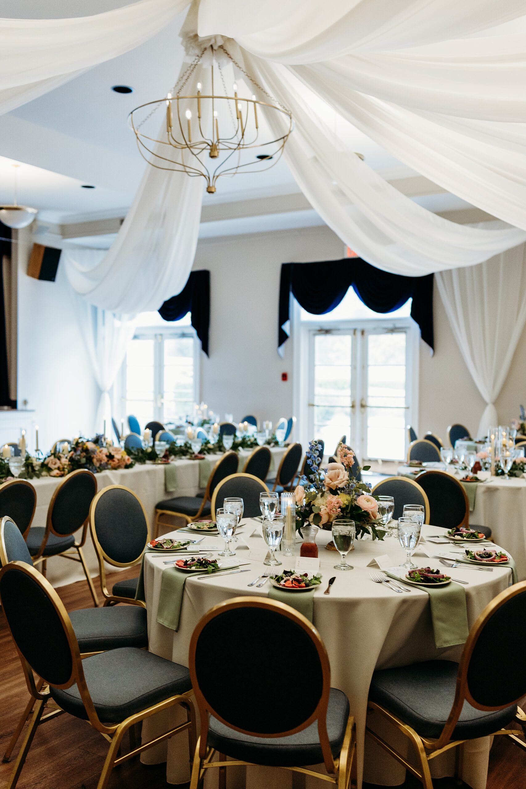 Draped ballroom tables set for a Gardencourt wedding reception with soft lighting and floral centerpieces in Hundley Hall.