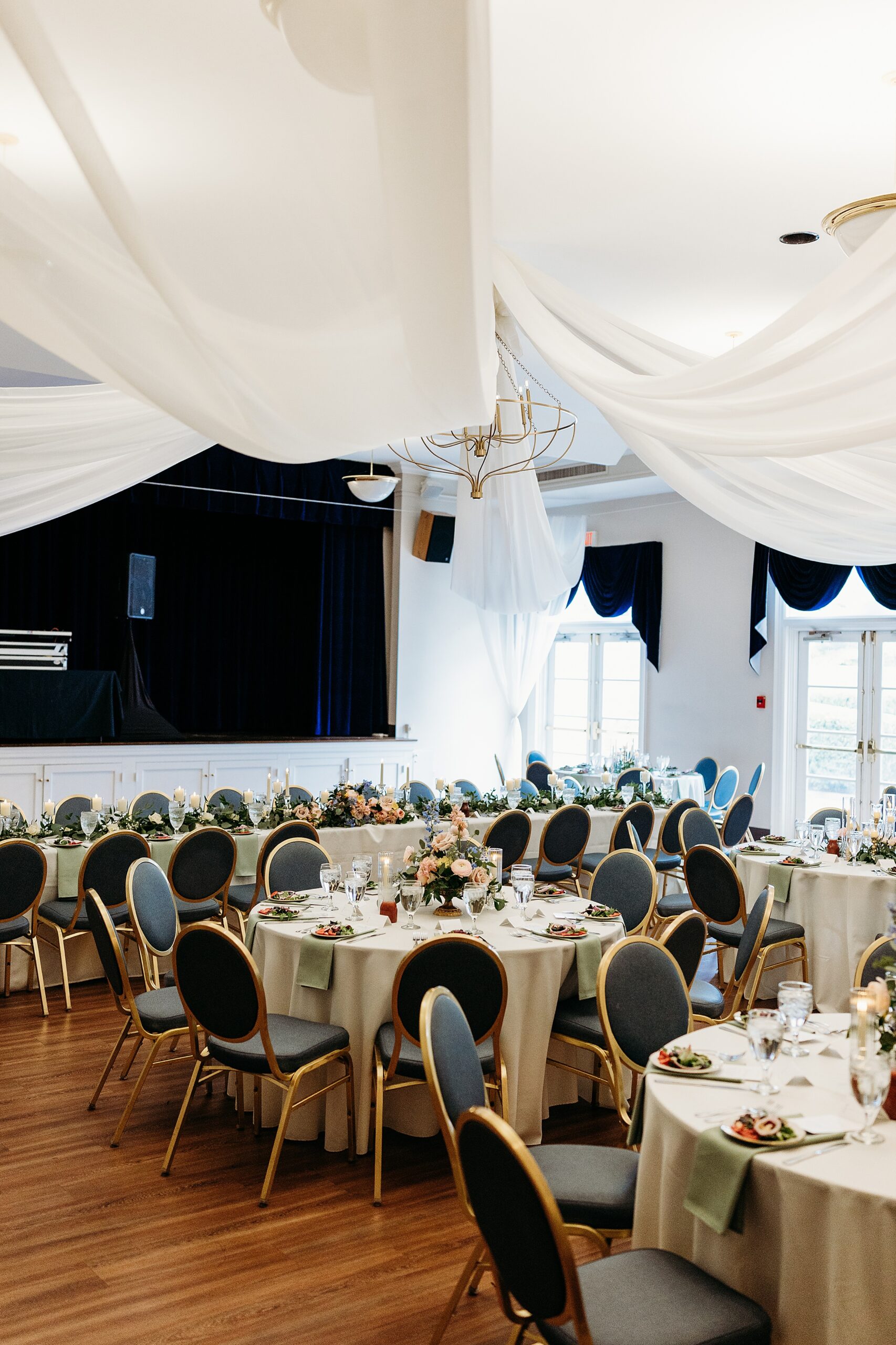 Wide view of the ballroom set for a Gardencourt wedding reception with draping and round tables