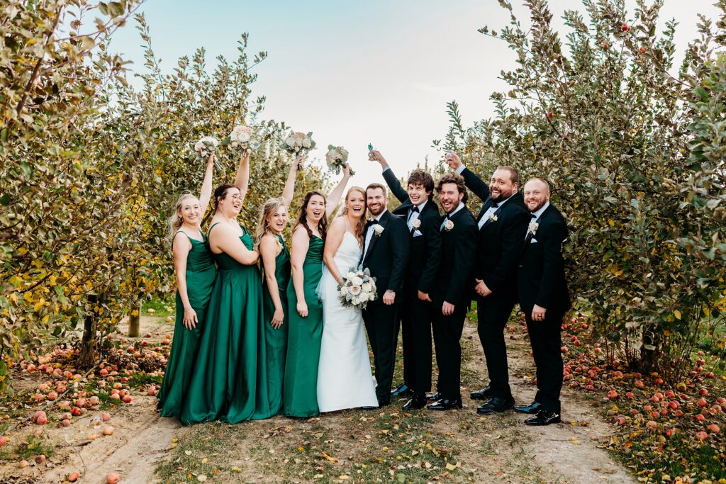 Bridal party celebrates in apple orchard at Hubers Orchard and Winery with bride and groom surrounded by bridesmaids and groomsmen