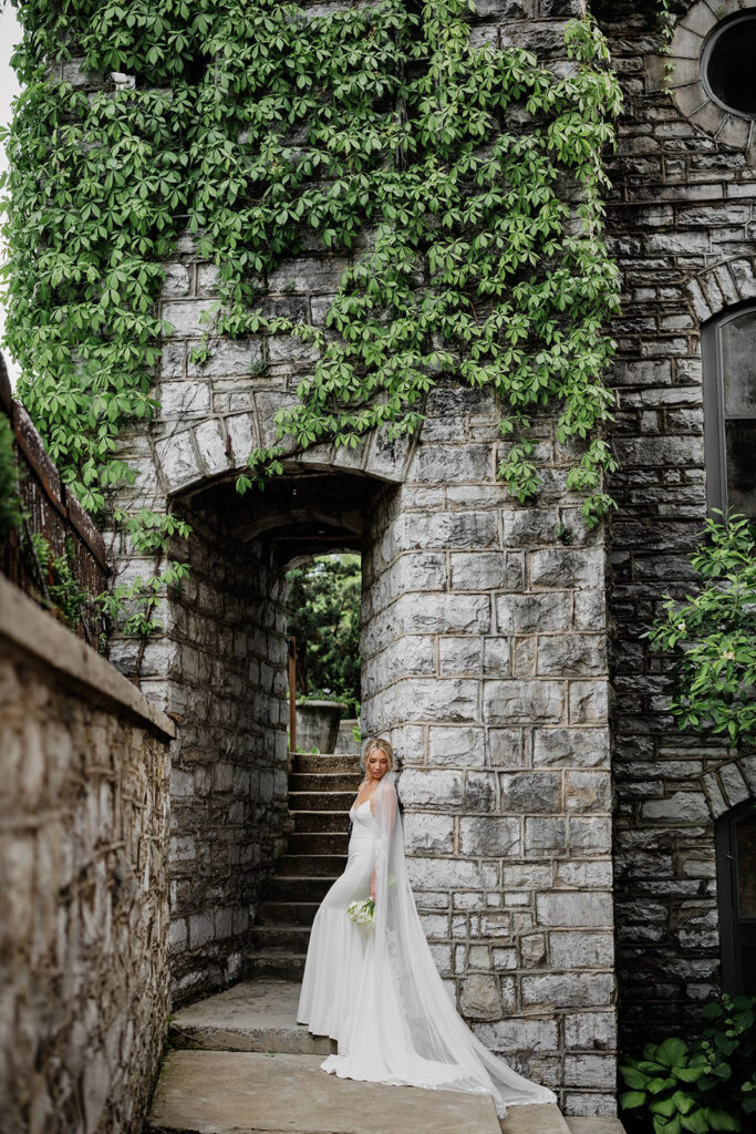 Castle & Key bridal portrait beside a historic stone archway covered in ivy and greenery.