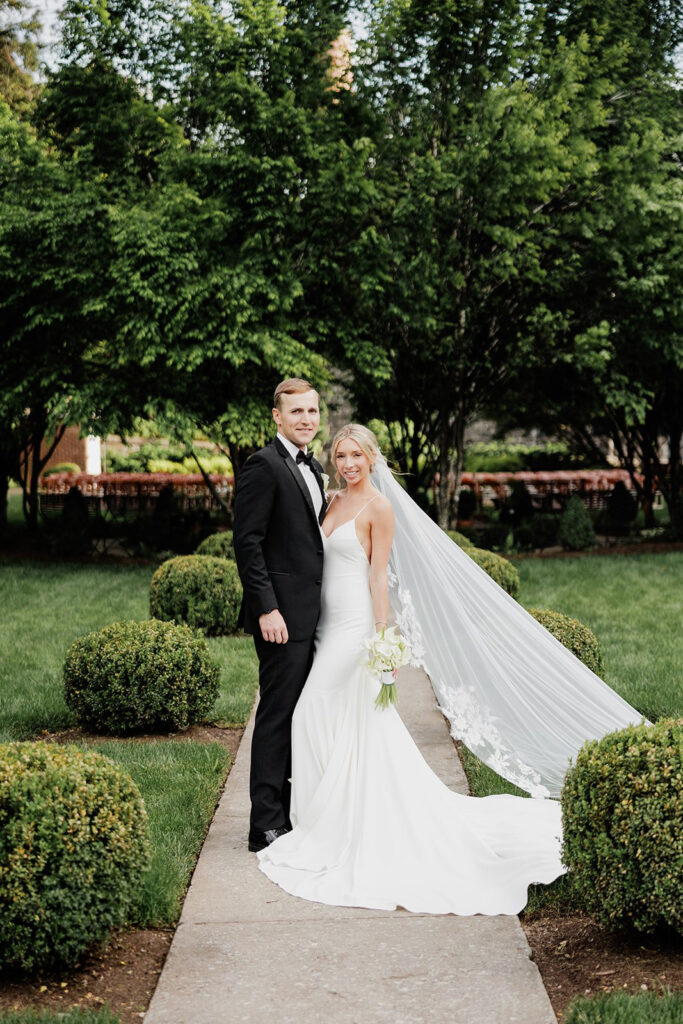 Castle & Key Sunken Garden wedding portrait of bride and groom standing along a garden pathway with the bride’s veil flowing behind her.