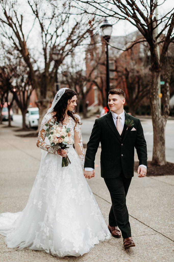 Bride and groom hold hands while walking together in downtown louisville