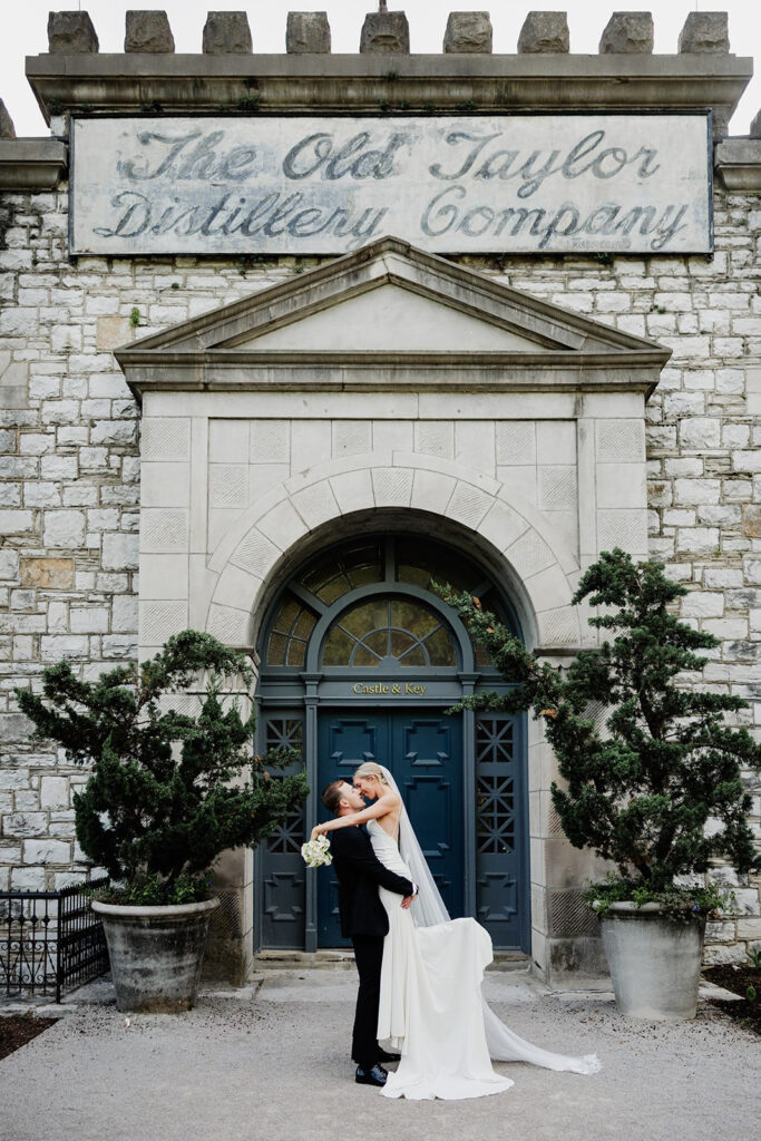 Castle & Key wedding portrait of groom lifting bride in front of the historic distillery entrance.