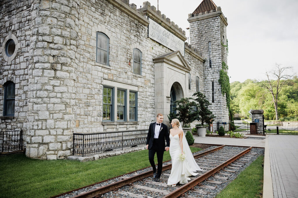 Castle & Key wedding couple walking along historic railroad tracks beside the distillery buildings.