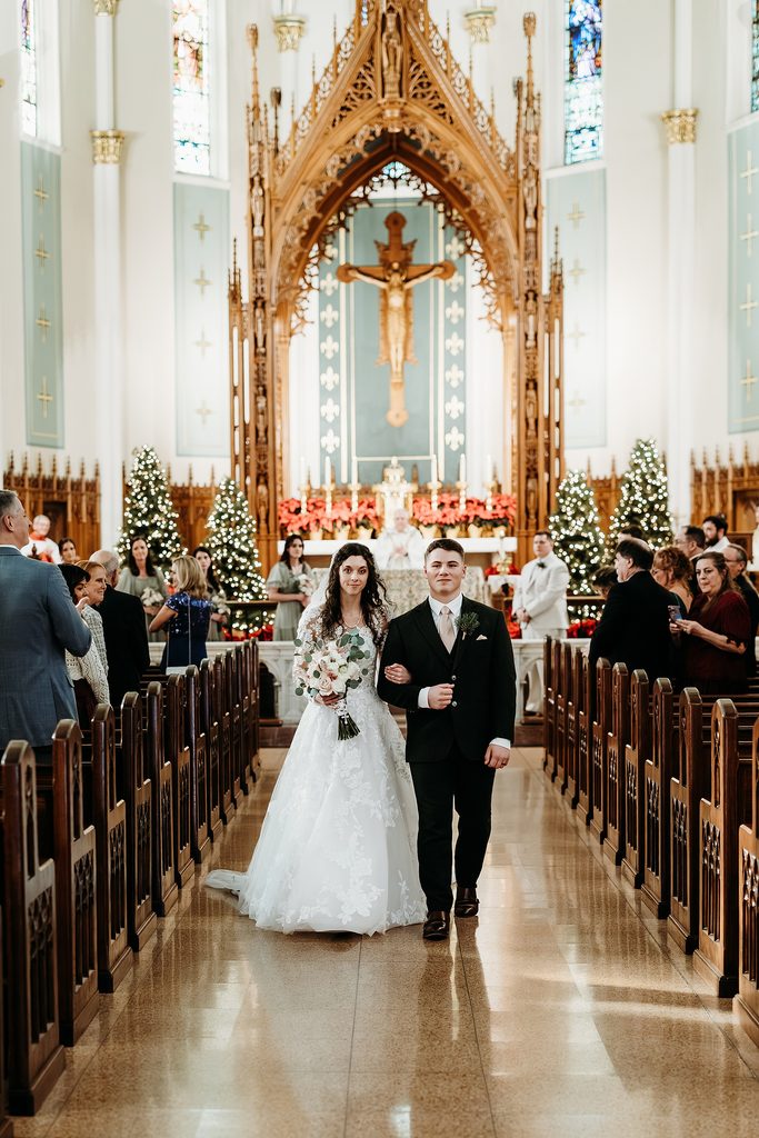 Newlyweds walking down the church aisle together after their Catholic wedding ceremony.