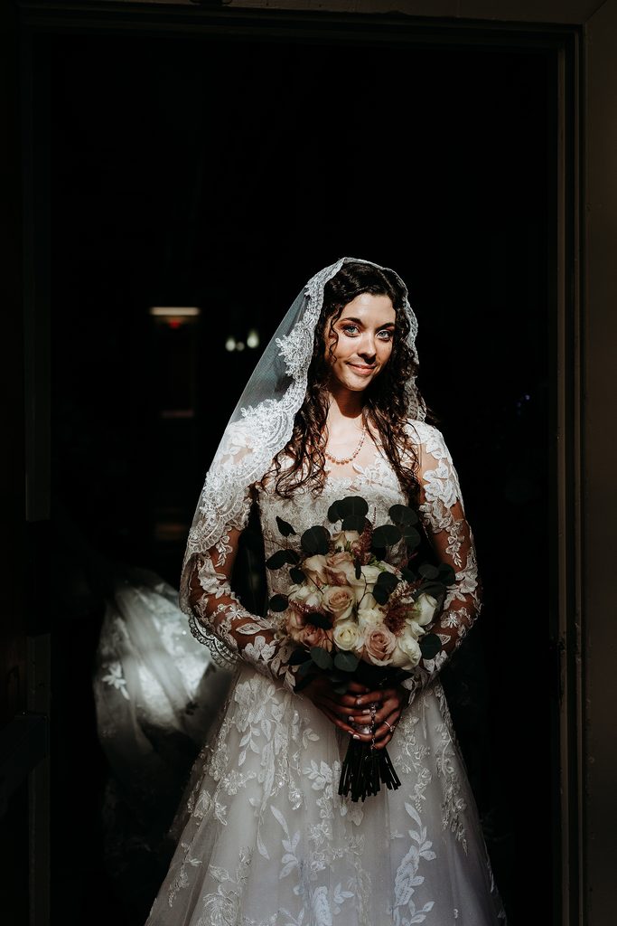 Bride in lace veil holding a rose bouquet before her St. Louis Bertrand Catholic Church wedding.