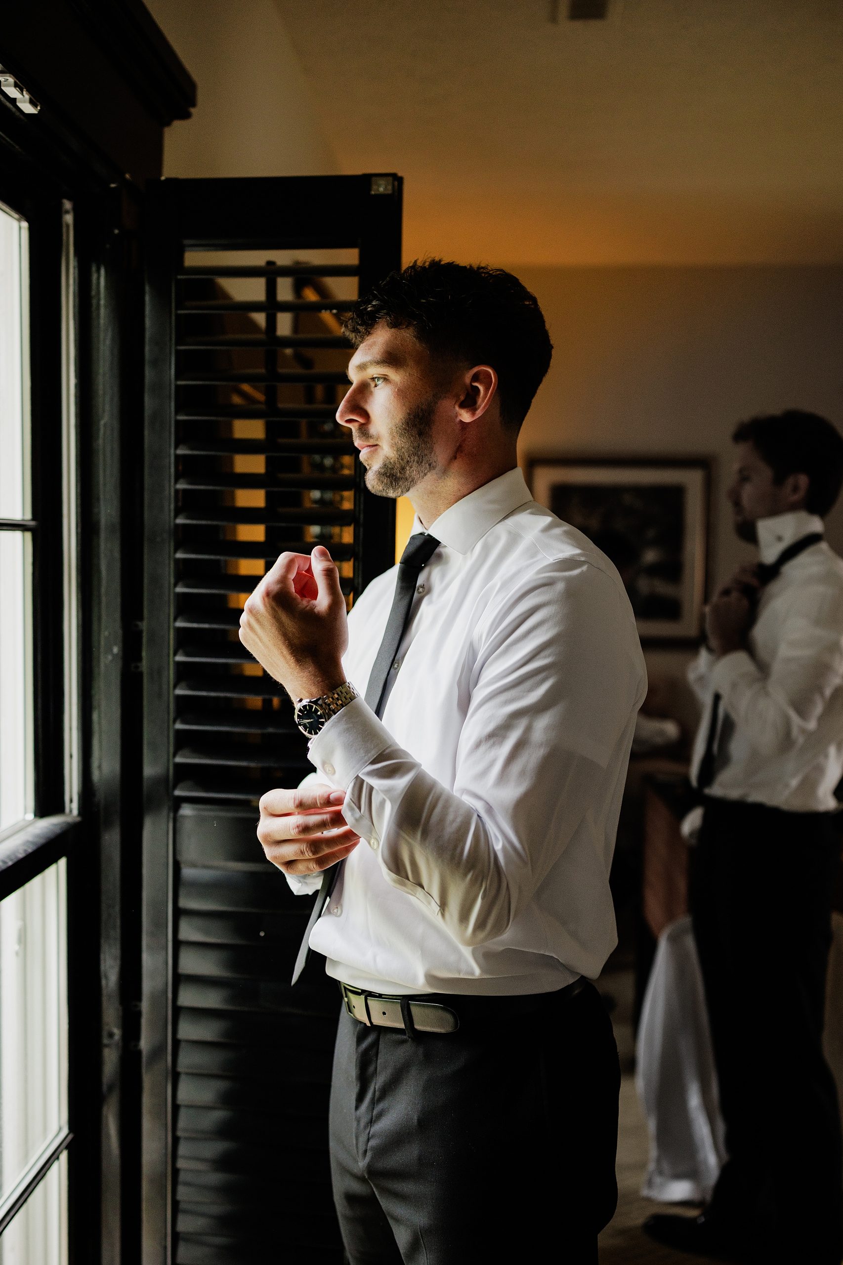 Groom adjusts his cuff while getting ready by a window at Bradshaw-Duncan House.