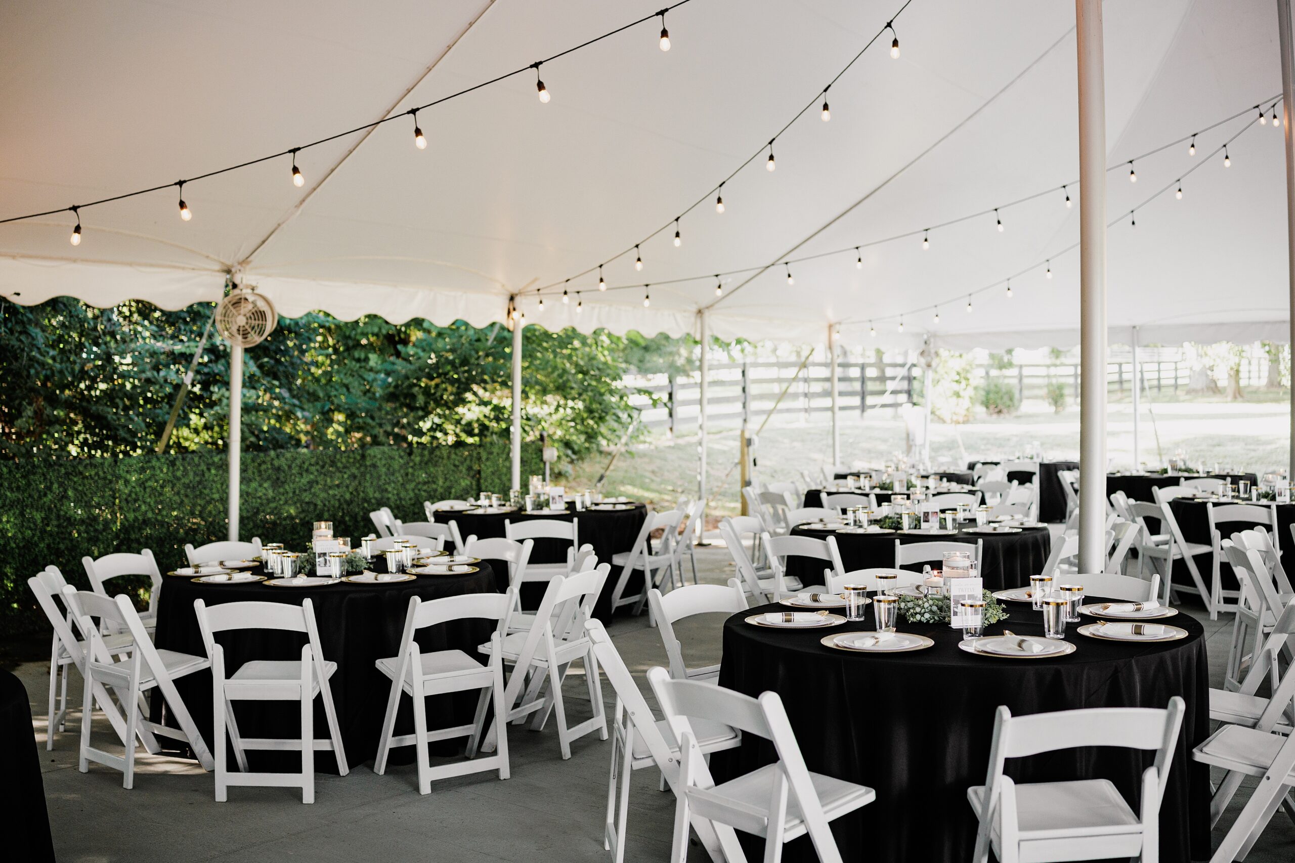 Tented wedding reception with black table linens, white chairs, candles, and string lights.