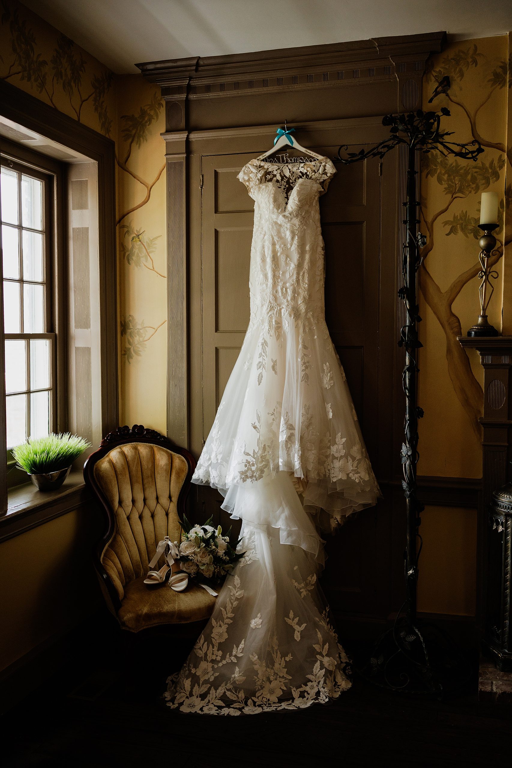 Lace wedding dress displayed inside Bradshaw-Duncan House with bridal shoes and bouquet.