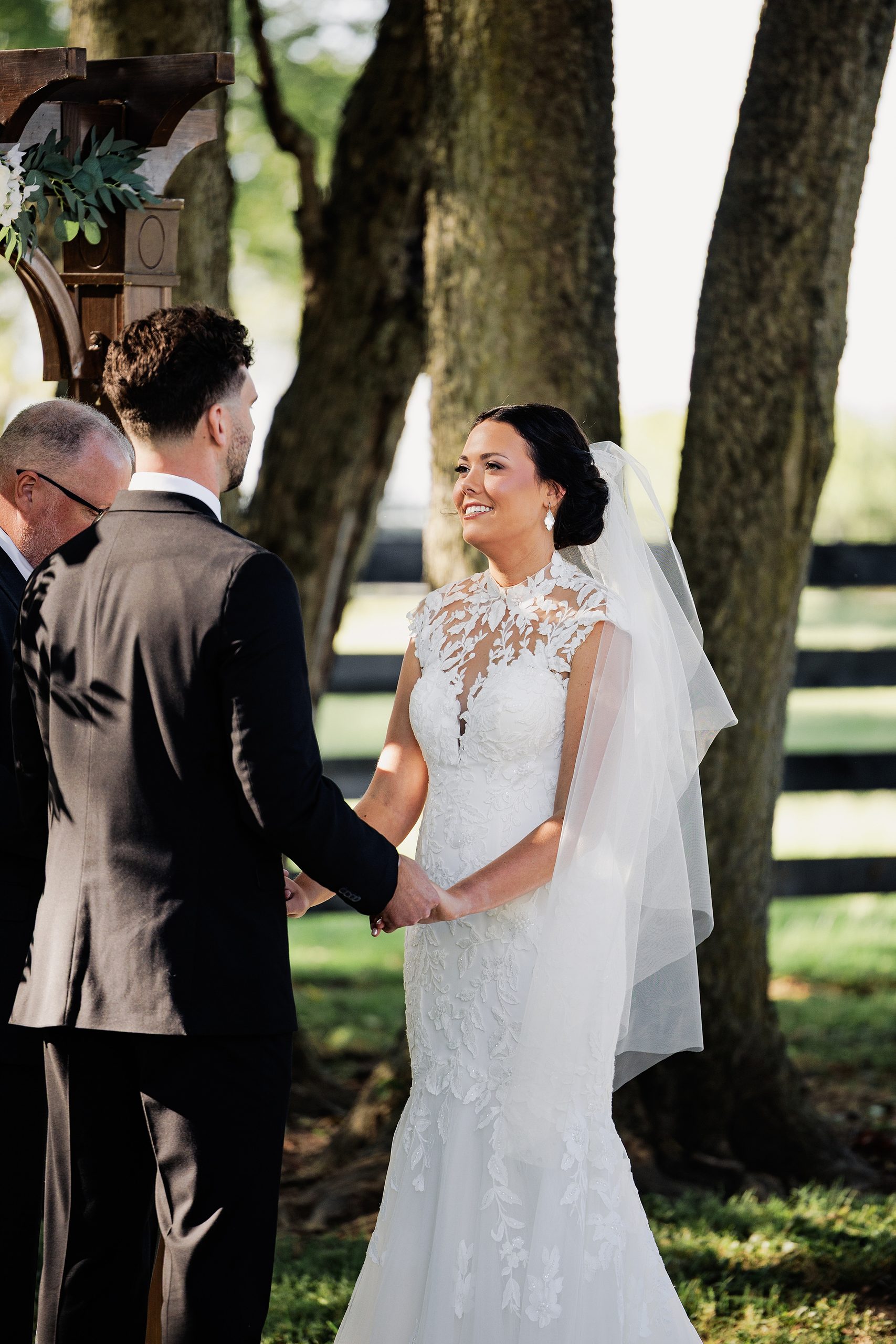 Bride smiles at the groom while holding hands during their outdoor wedding vows.