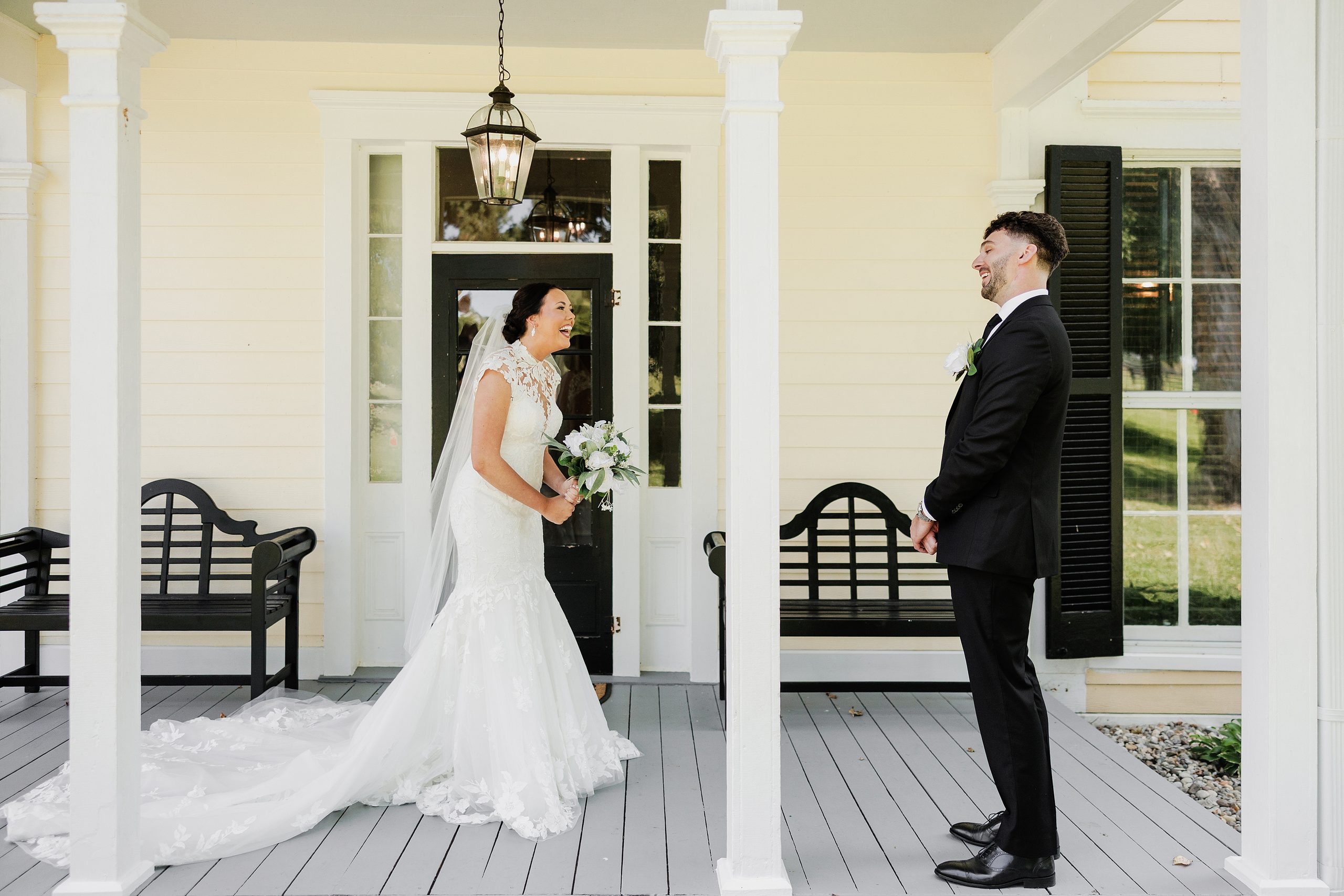 Bride and groom laugh together during their wedding first look on the porch.