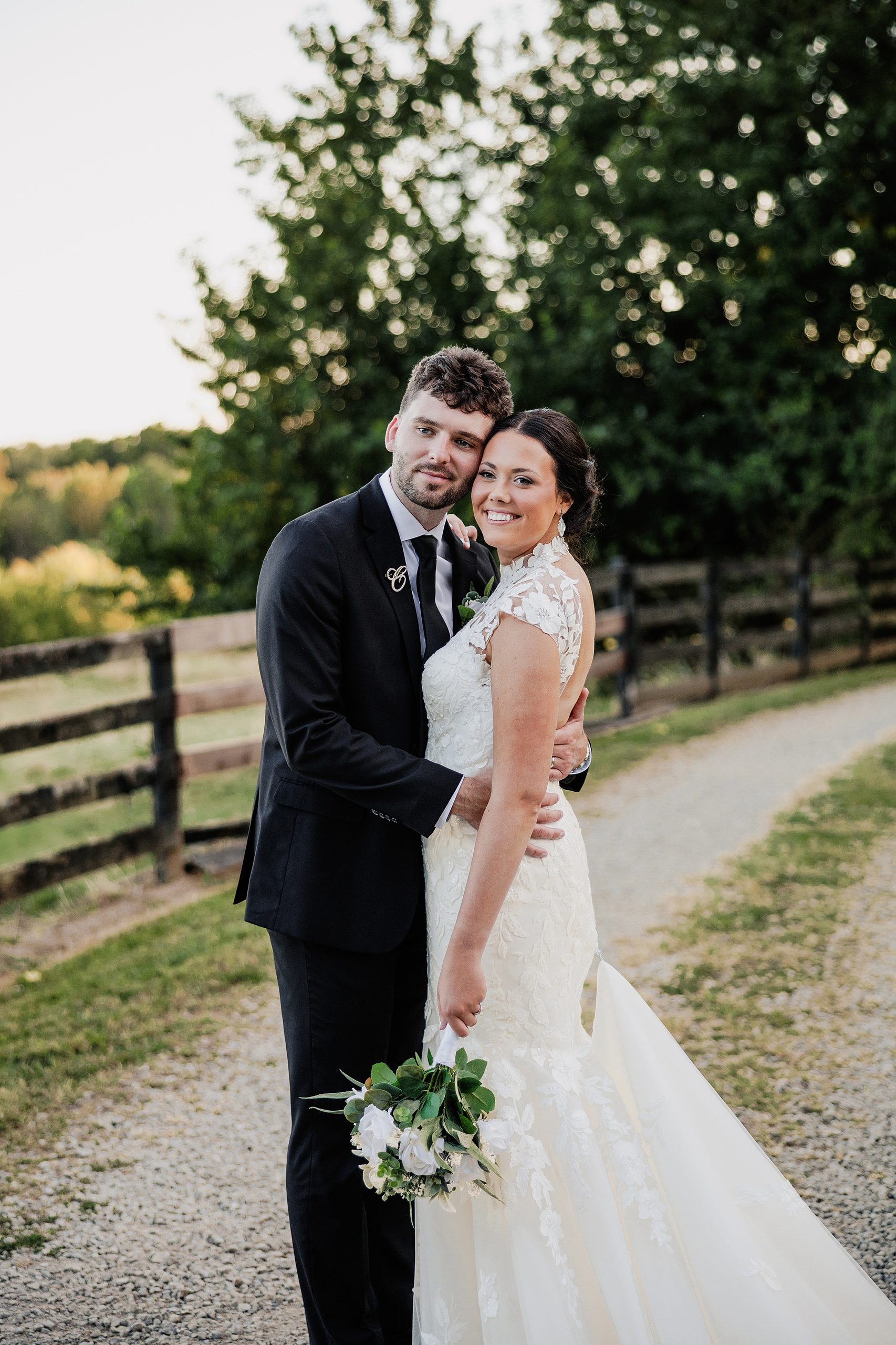 Bride and groom embrace for an outdoor wedding portrait beside a rustic wooden fence.