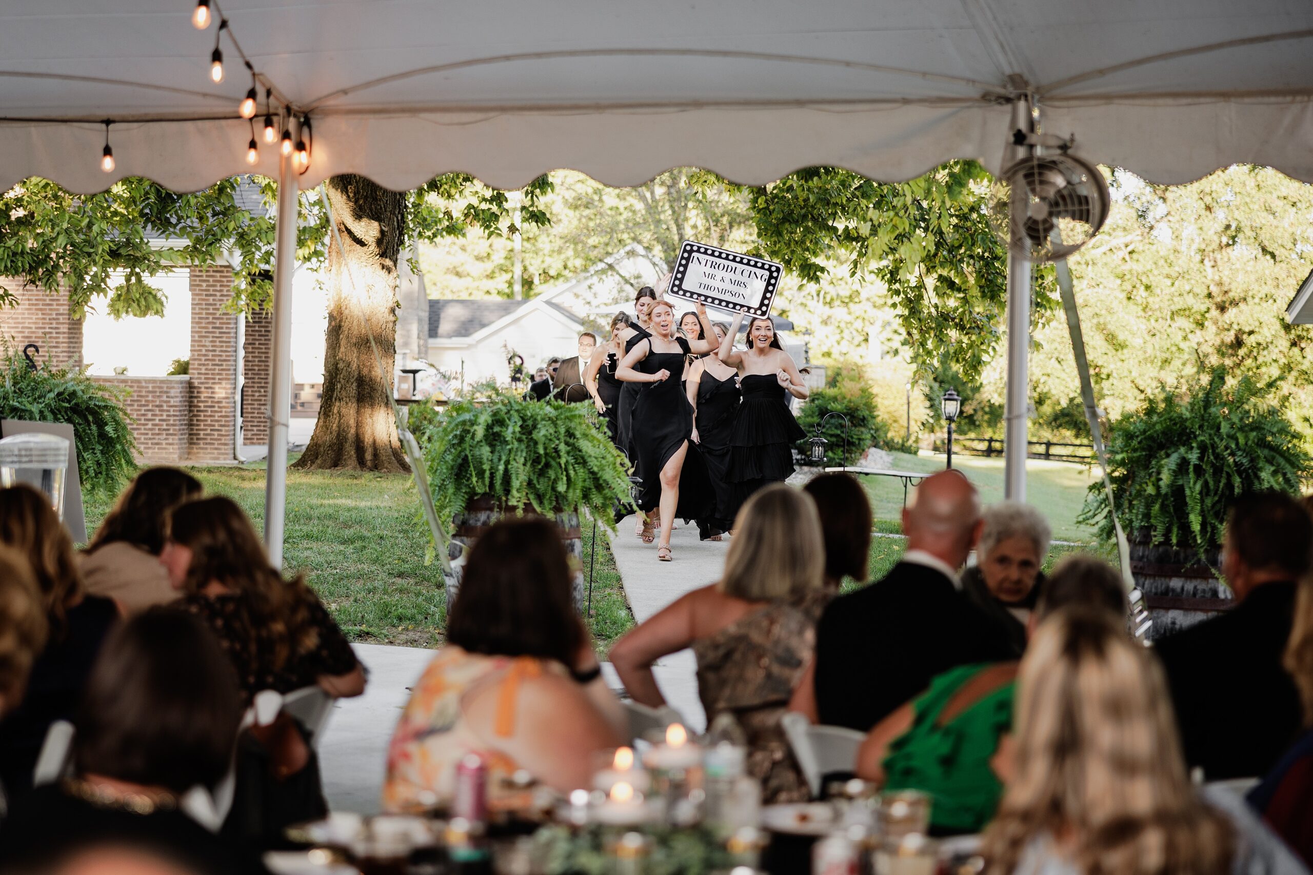 Bridesmaids in black dresses make a lively entrance into the tented wedding reception.