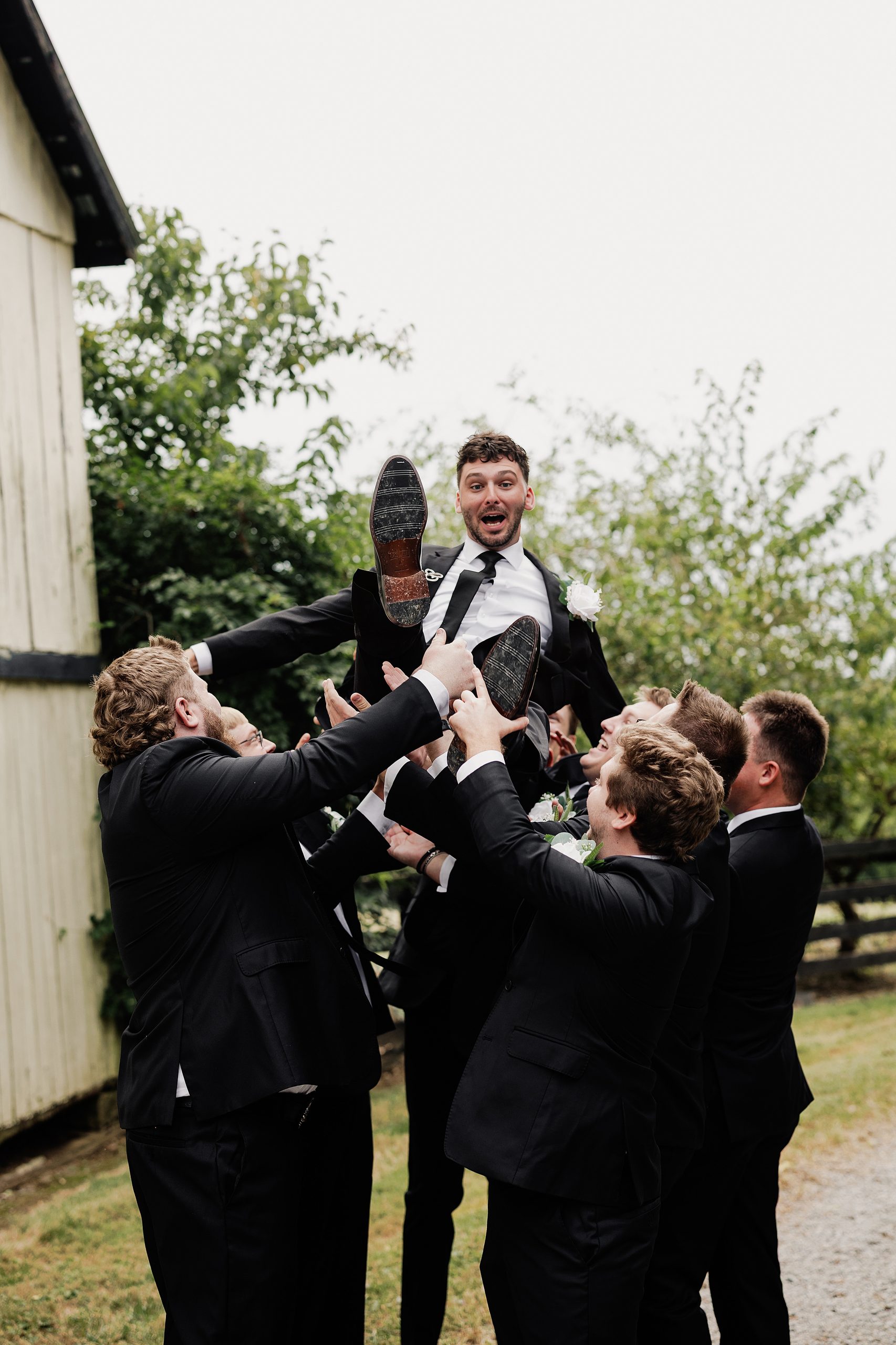 Groomsmen toss the groom into the air during a playful wedding party portrait.