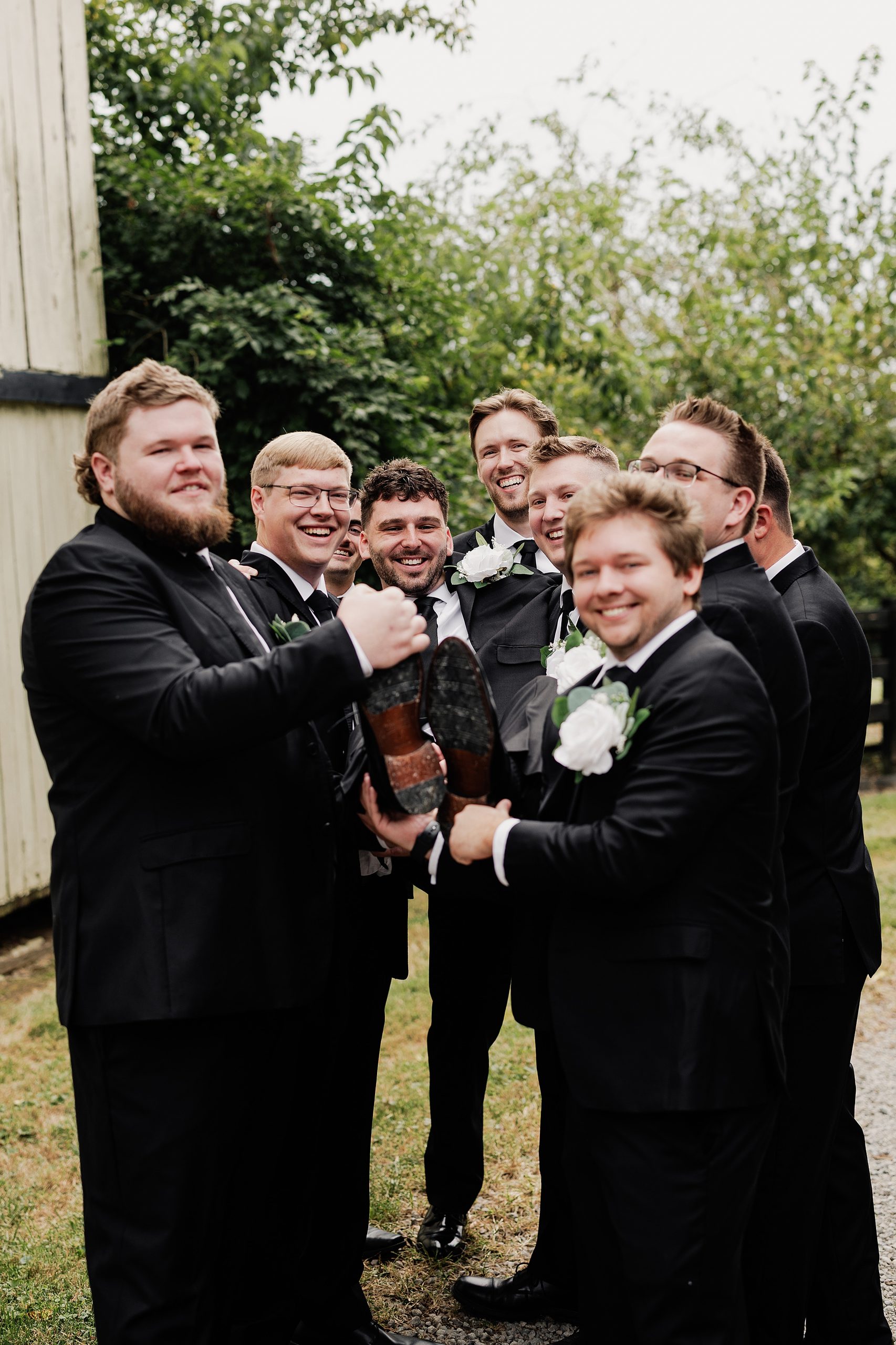 Groomsmen laugh together while preparing to lift the groom during wedding party portraits.