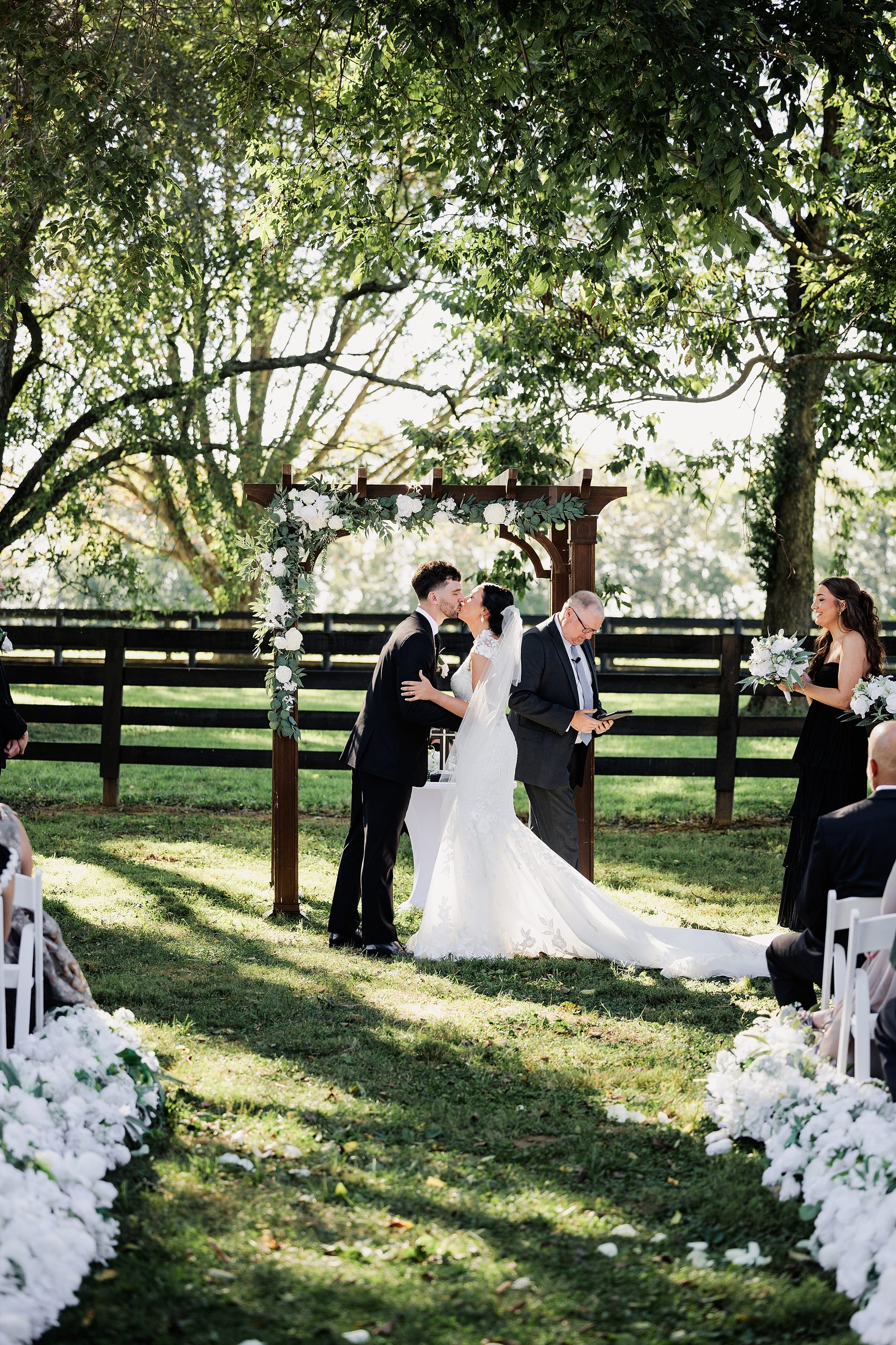 Newlyweds share their first kiss beneath a floral arbor at their outdoor wedding ceremony.