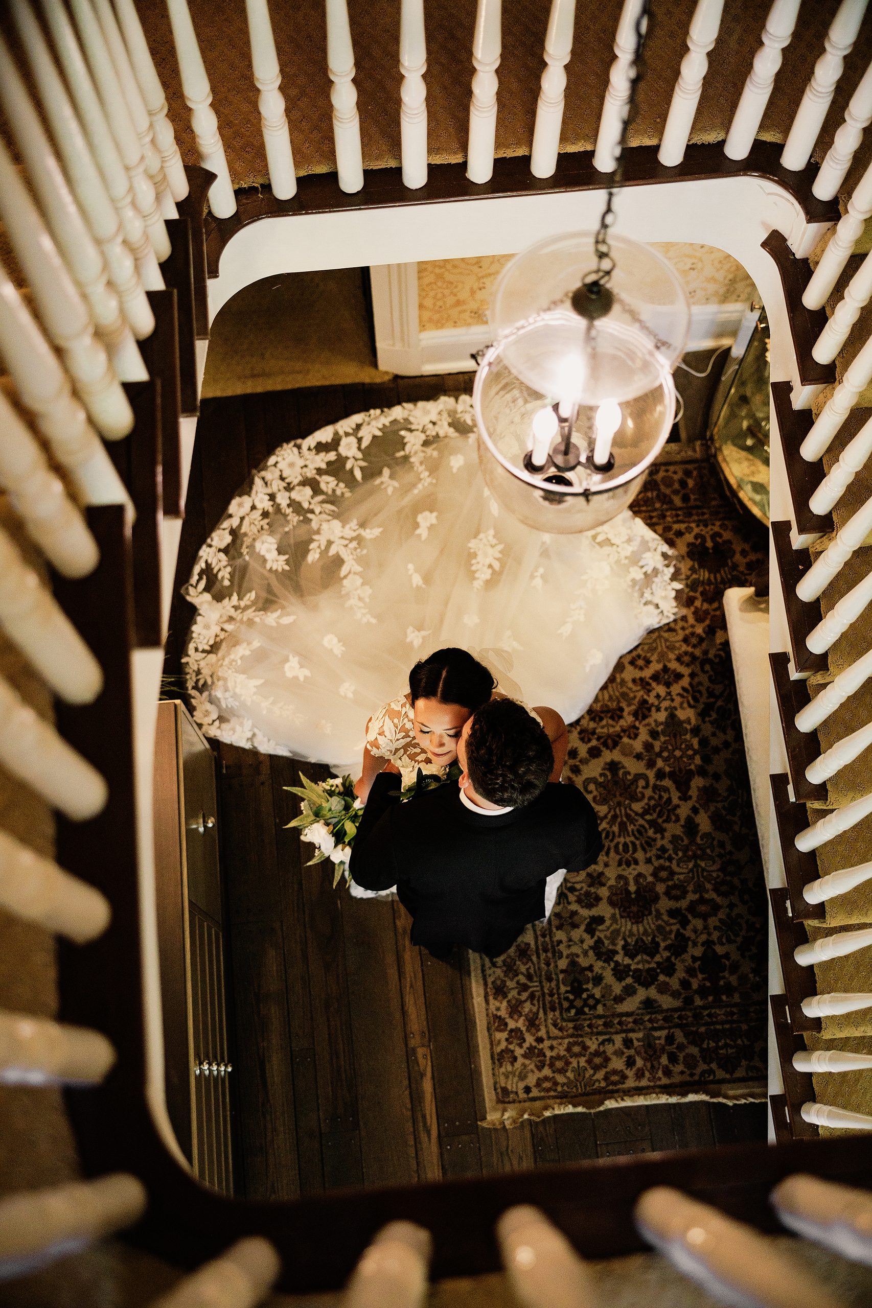 Overhead portrait of the bride and groom beneath a chandelier on a historic staircase.