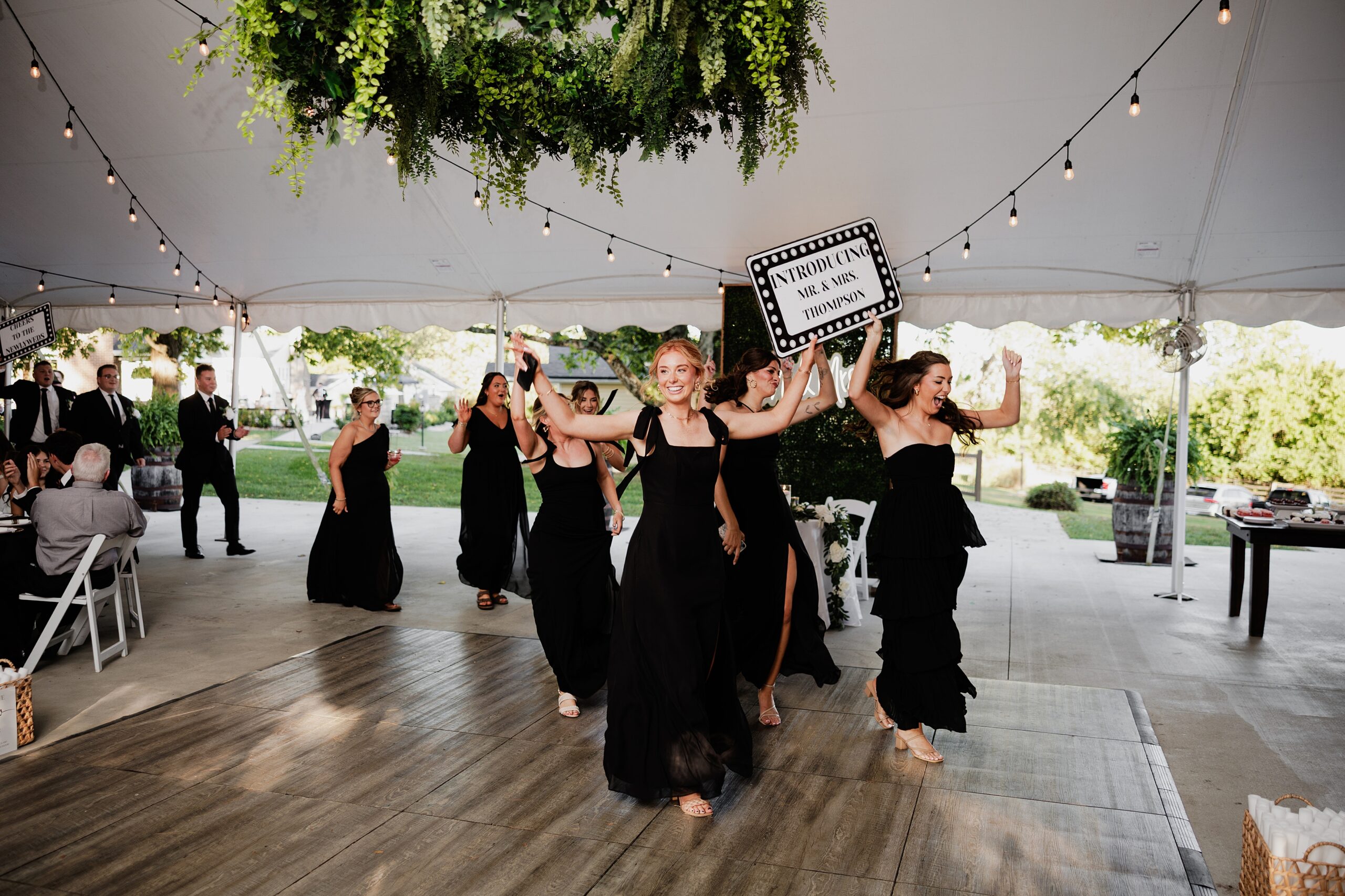 Wedding party celebrates during a grand entrance beneath hanging greenery and string lights.