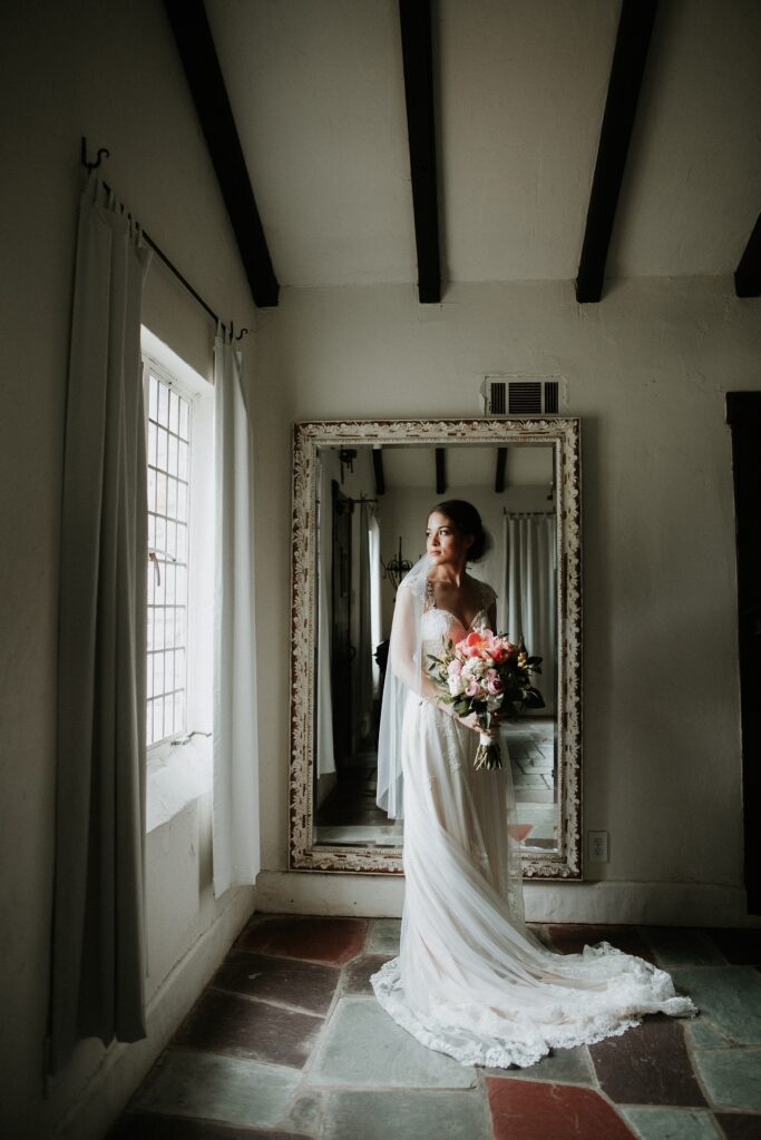 Yew Dell bride holding her bouquet during a bridal portrait by a window with a vintage mirror in the background.