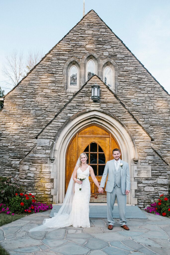 Bride and groom holding hands in front of a stone chapel entrance after their wedding ceremony