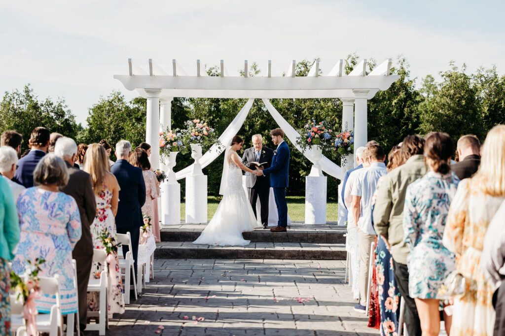 Bride and groom hold hands during prayer at their outdoor patio ceremony at Huber's Winery