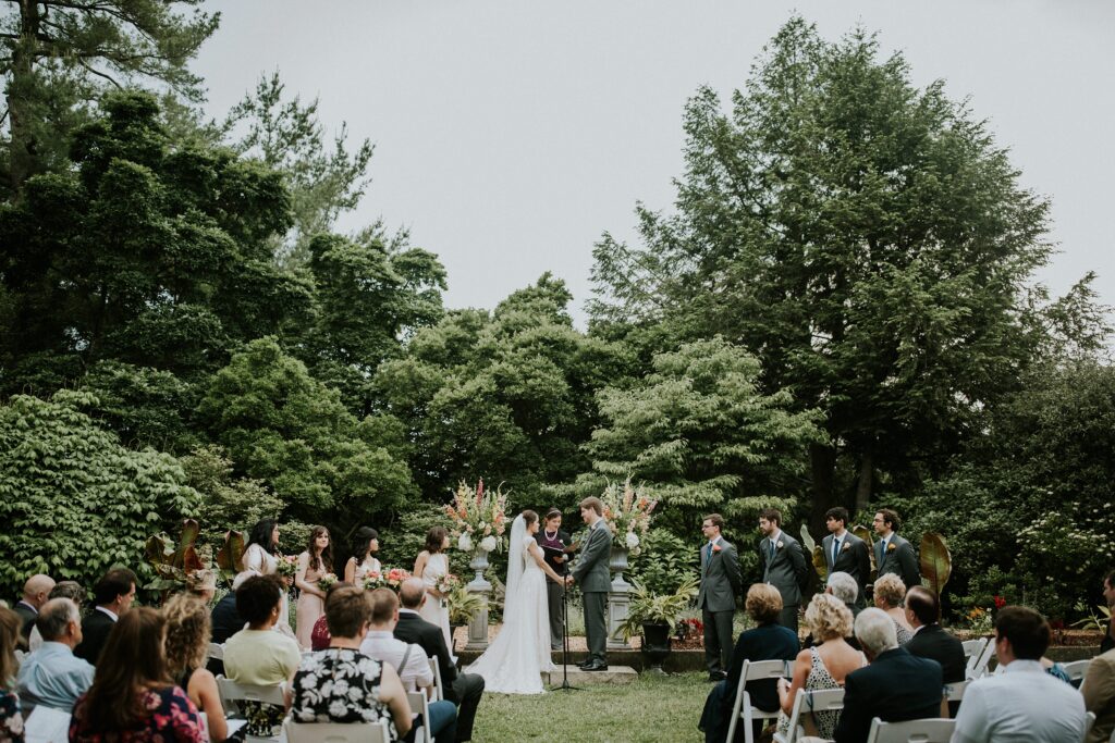 Yew Dell wedding ceremony on the Event Lawn with guests seated as the couple exchanges vows surrounded by lush gardens and floral arrangements.