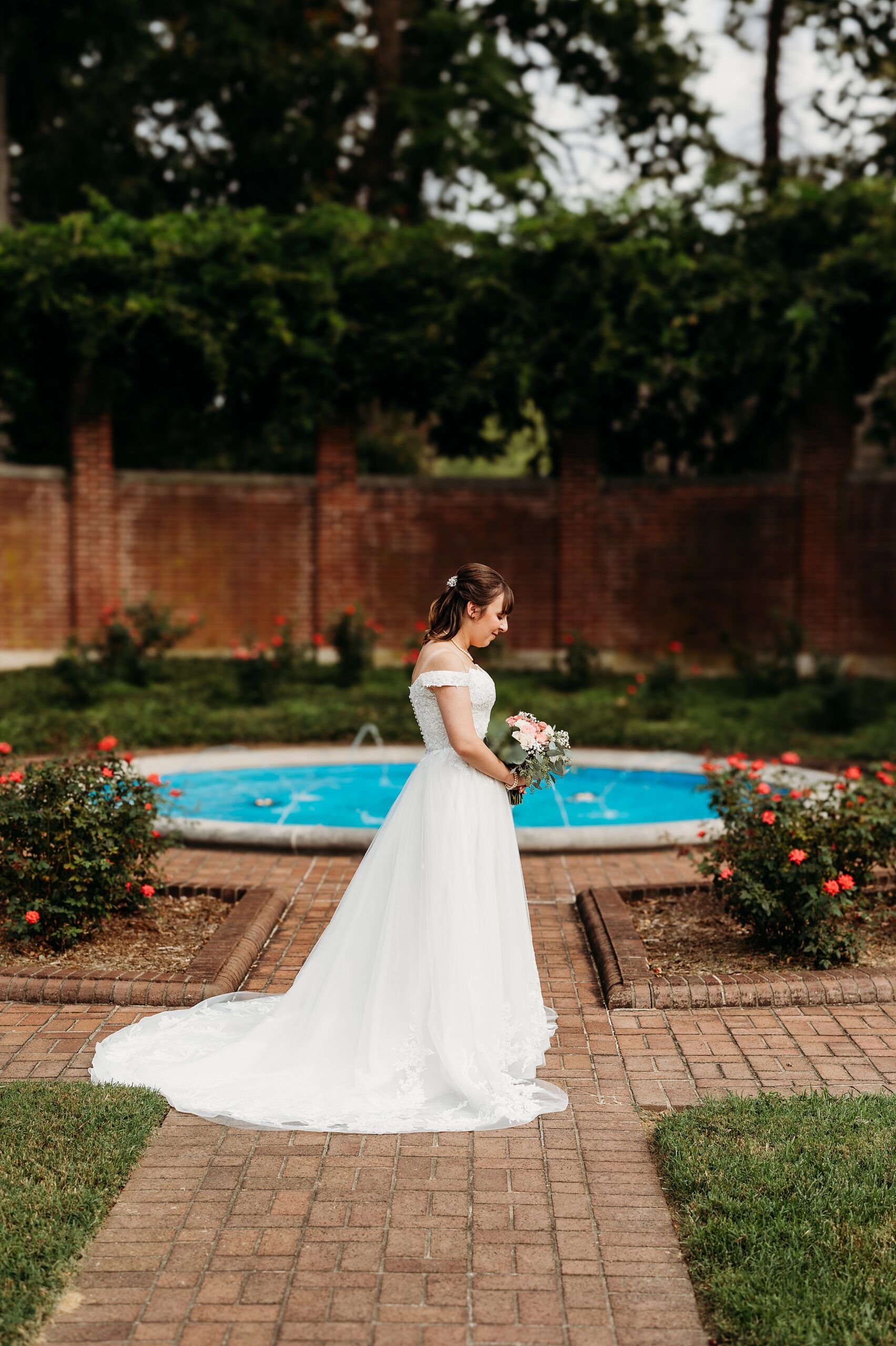 Gardencourt bride standing beside the fountain garden with blooming roses and brick pathways.