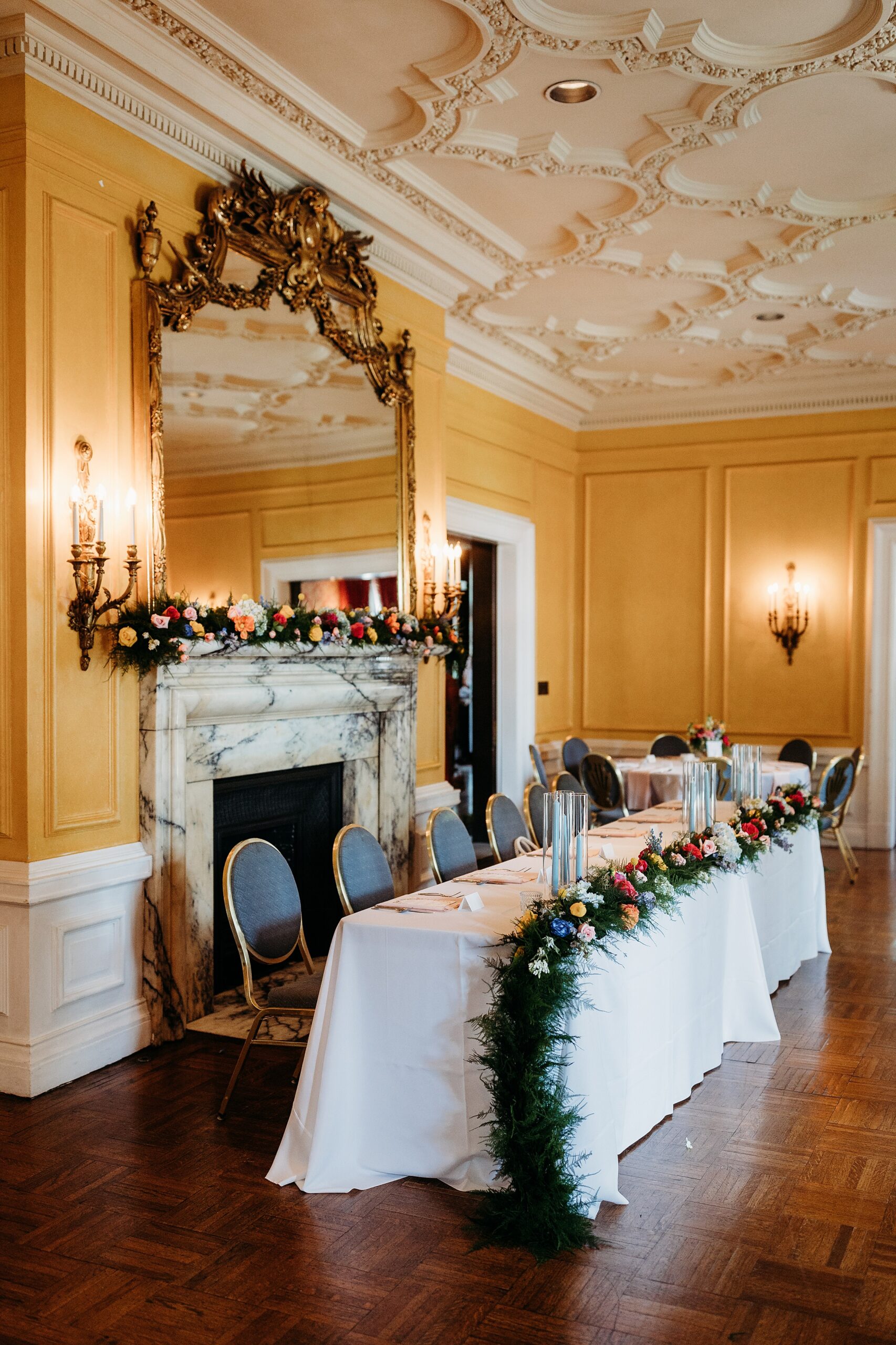 Garden Court head table with floral garland, marble fireplace, ornate mirror, and elegant wedding reception decor.