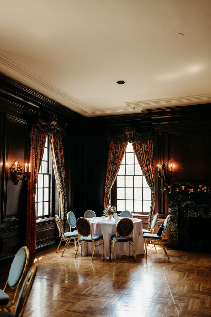Reception room with wood paneled walls, a marble fireplace, and elegant wedding reception table setup.