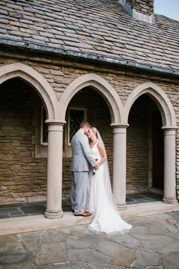 Bride and groom sharing a quiet embrace beneath stone arches in a timeless wedding portrait