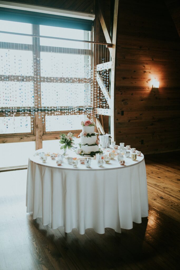 Yew Dell Gheens Barn wedding cake display with a three tier floral cake, candles, and hanging origami crane backdrop.