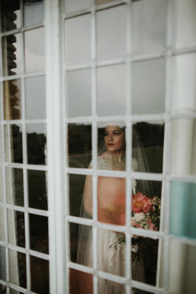 Yew Dell bridal portrait through a window with the bride holding her bouquet and looking out across the gardens.
