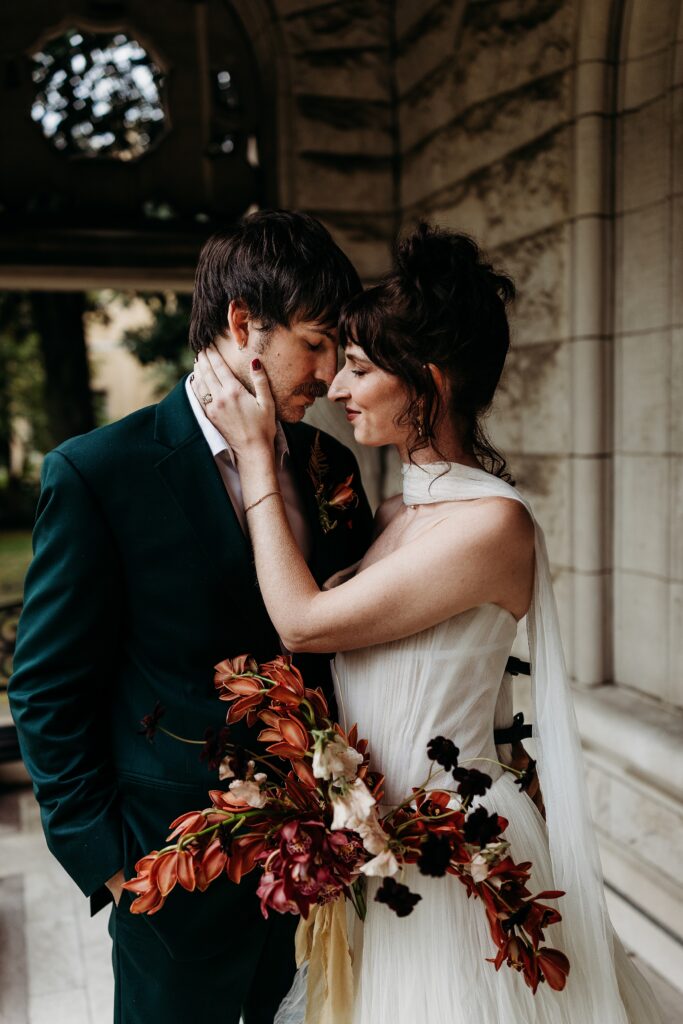 Couple embraces beneath the stone archway with dramatic florals.