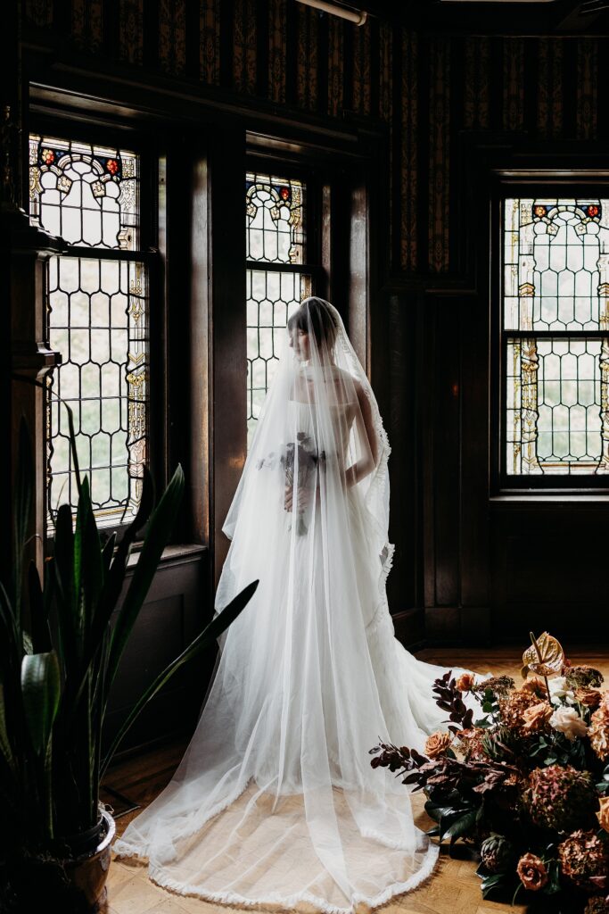 Bride stands beneath her veil beside stained glass windows inside historic house in louisville, KY