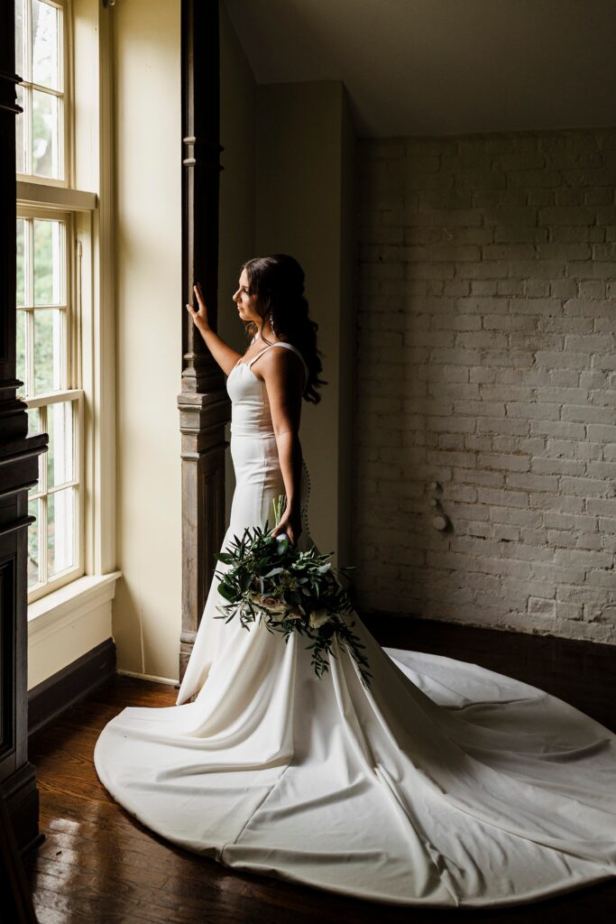 Natural window light highlights a bride holding her bouquet inside a historic home in Louisville, KY