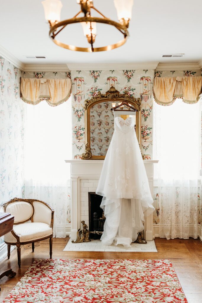 Louisville bridal suite with a wedding dress hanging in front of an ornate fireplace and vintage mirror.