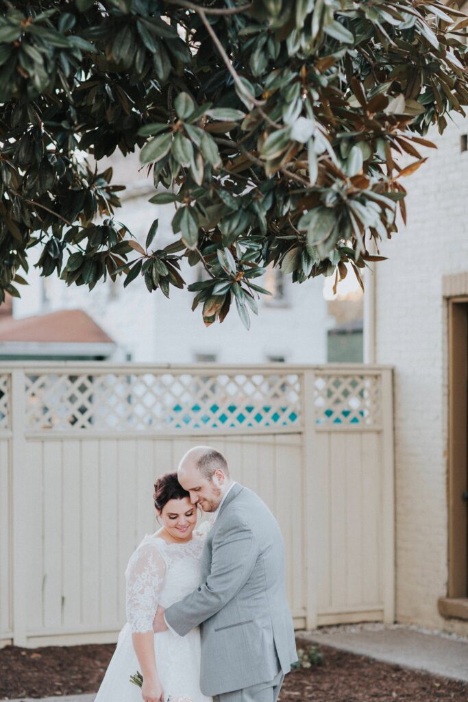 Bride and groom embracing beneath a magnolia tree after their small wedding ceremony.