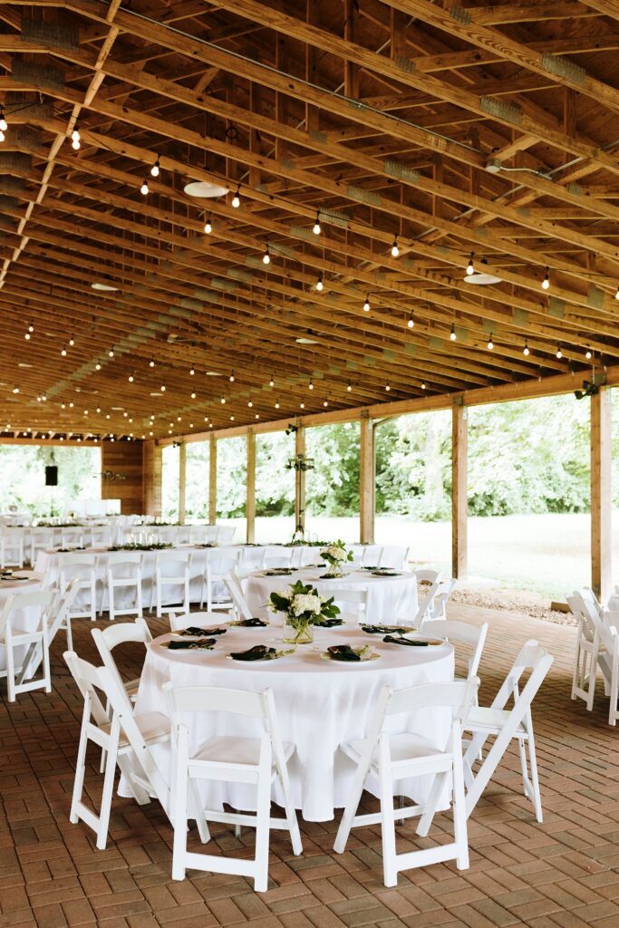 Covered outdoor reception pavilion with string lights, elegant tables, and white chairs.