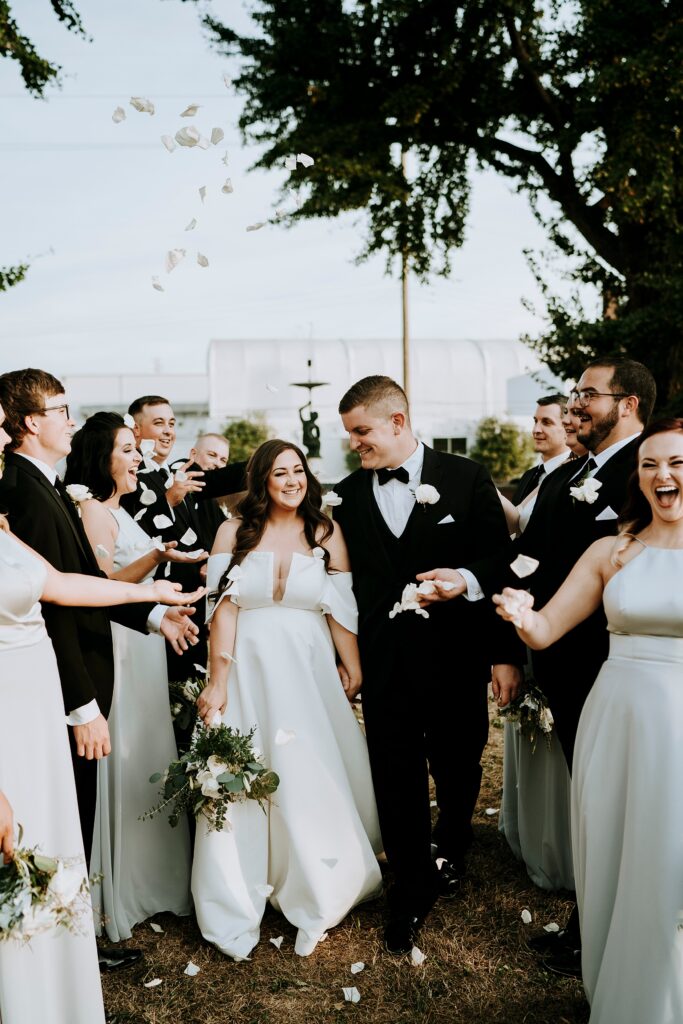 Wedding party tosses flower petals as newlyweds celebrate outside.