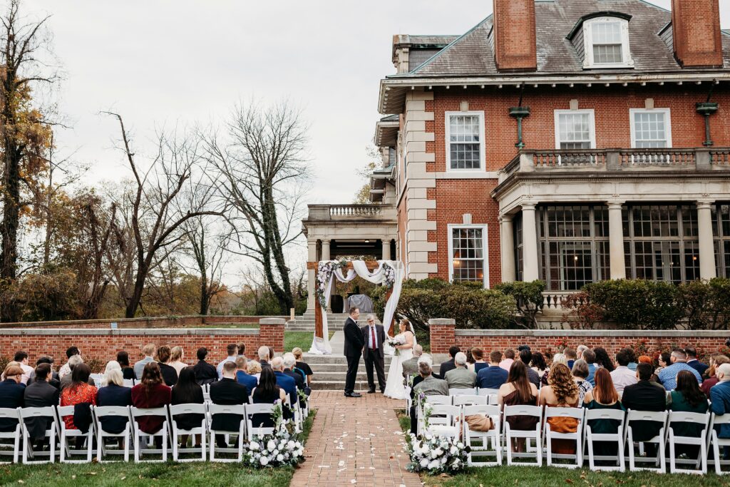 Small outdoor fall wedding ceremony in front of the historic Gardencourt mansion with guests seated on the lawn.