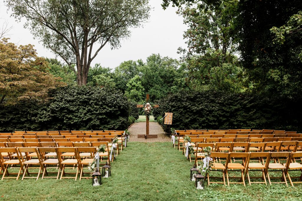An outdoor ceremony setup at features rows of wooden chairs leading to a floral cross in the garden ceremony space.