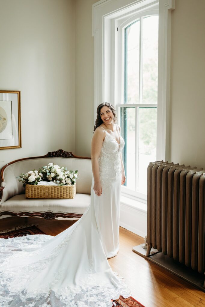 Bridal portrait by a tall window with natural light and a flowing wedding dress.