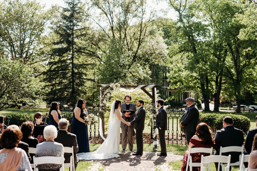Intimate outdoor wedding ceremony in the garden with a floral arbor and seated guests.