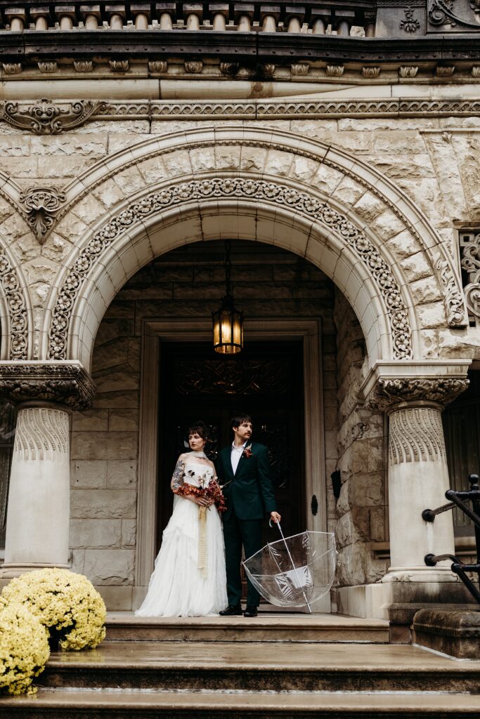 Couple poses beneath the ornate historic entrance on a rainy wedding day in Louisville.