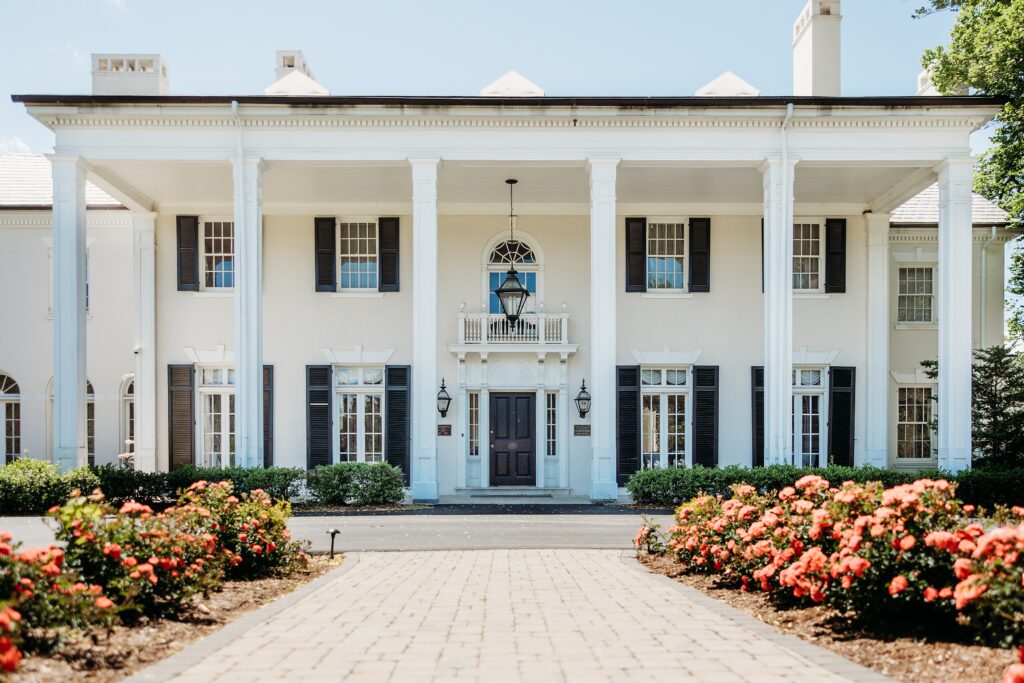 Front exterior of the Tway House surrounded by blooming roses and white columns.
