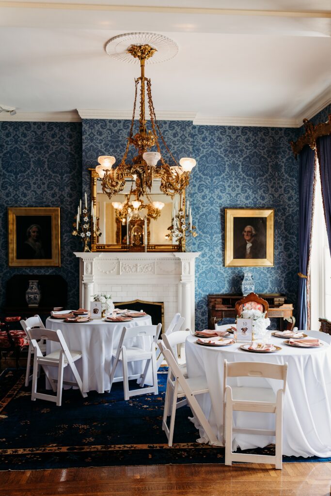 Small Louisville wedding reception setup in the Blue Parlor with round tables, a fireplace, blue wallpaper, and an ornate chandelier.