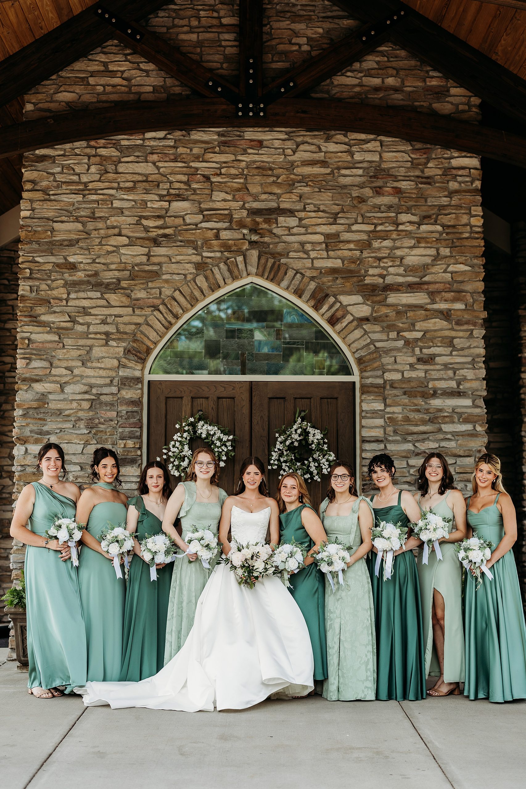 Bride and bridesmaids standing with their bouquets in front of the doors of Chapel in the Woods.