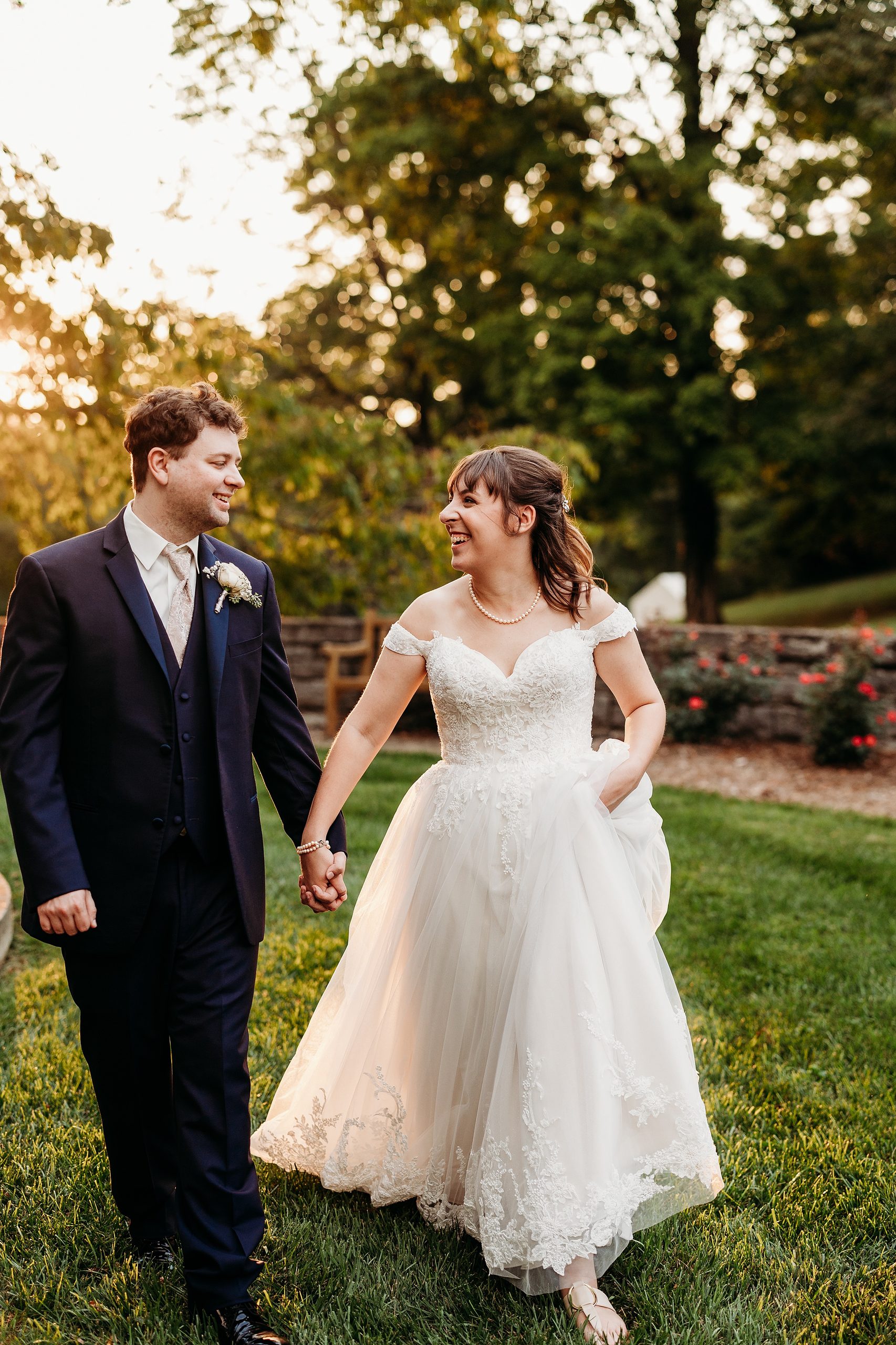 Bride and groom laughing together while walking hand in hand during sunset wedding portraits.