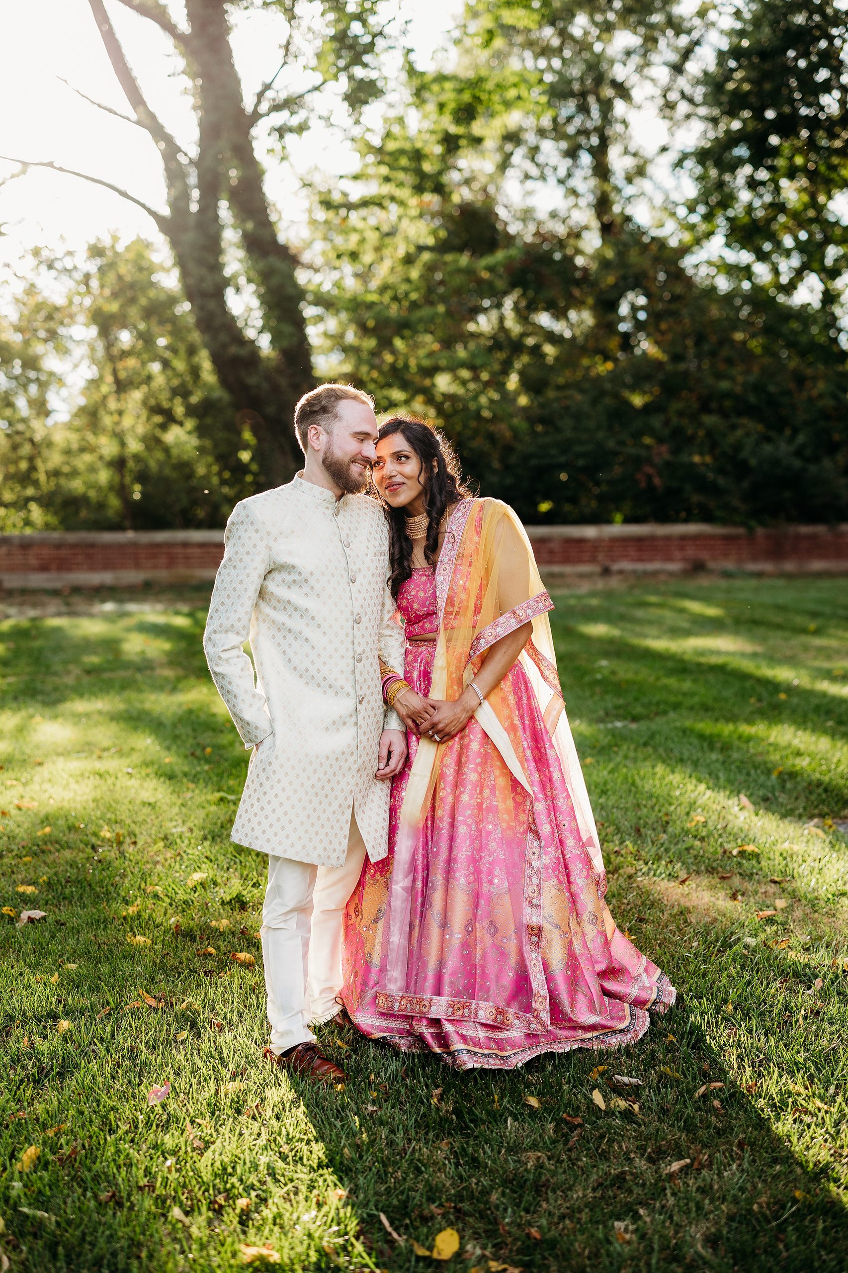 Couple in colorful traditional Indian wedding attire share a quiet moment outdoors in the evening light.