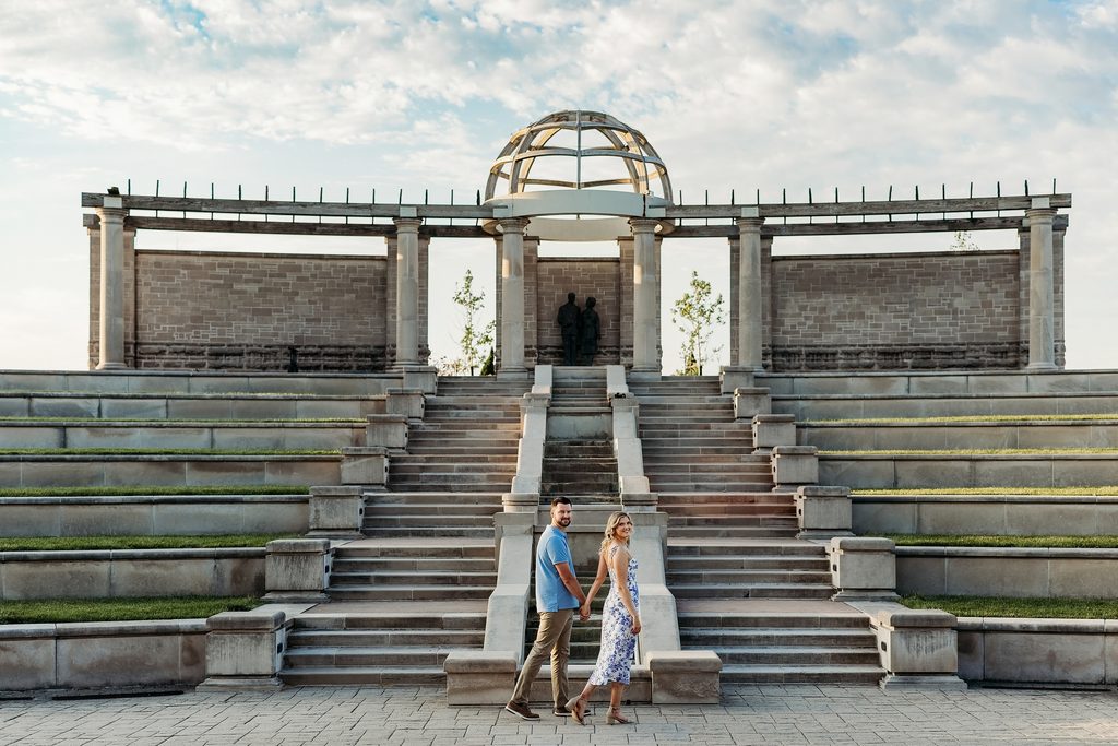 Engaged couple holding hands in front of the stone steps at Coxhall Gardens.